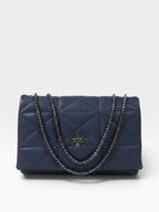 A navy blue Prada quilted leather shoulder bag with a silver-tone chain strap and a central metal logo plaque.