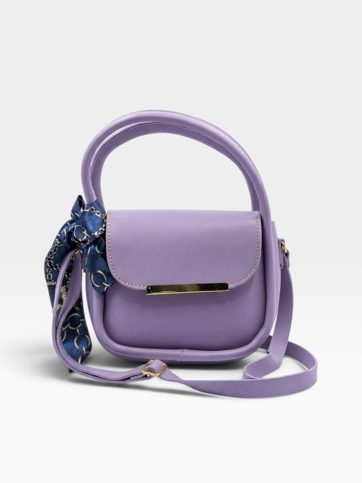 A lavender purple top-handle crossbody bag with a matching shoulder strap, a gold-tone metal bar on the front, and a blue patterned silk scarf tied to the side, shown on a light gray background.