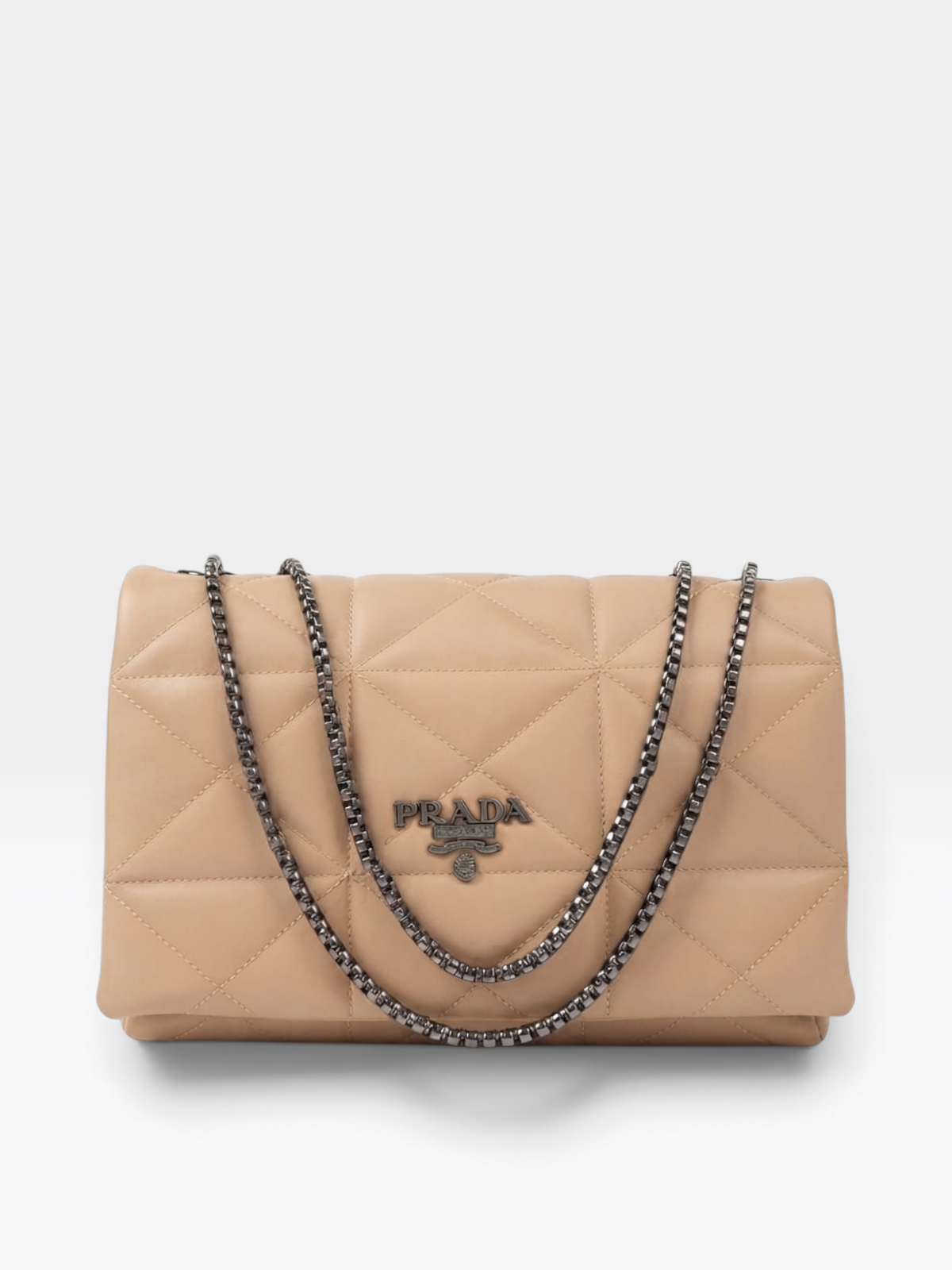Prada quilted flap shoulder bag in beige leather with a silver-tone chain strap and a silver-tone Prada logo plaque on the front, photographed on a light gray background.