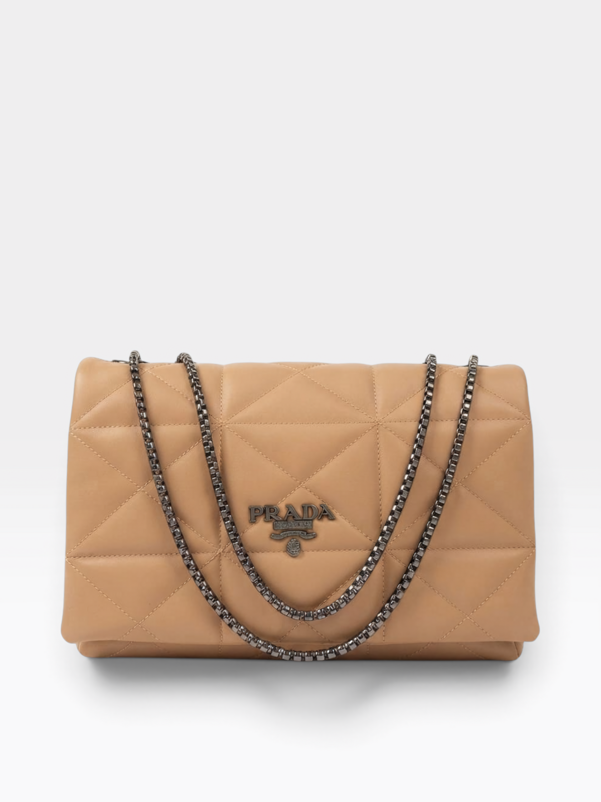 A Prada quilted shoulder bag in tan leather with a silver-tone chain strap and a silver-tone metal logo plaque on the front, set against a light gray background.