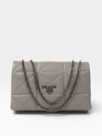 A Prada quilted shoulder bag in light gray leather with a silver-tone chain strap and a central Prada logo plaque, photographed against a clean white background.