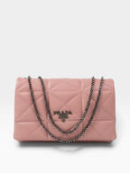 A pink quilted Prada shoulder bag with a silver-tone chain strap and a silver-tone metal logo plaque on the front, set against a plain light gray background.